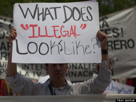Person holding sign asking "What does illegal look like?"